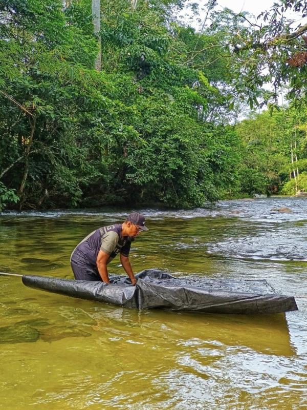 After breaking camp, Adly lashes a rope across the shallow river to hold the soiled groundsheet for washing.