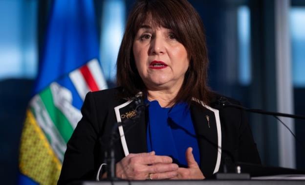 A woman with a black suit and blue blouse stands at a podium. 