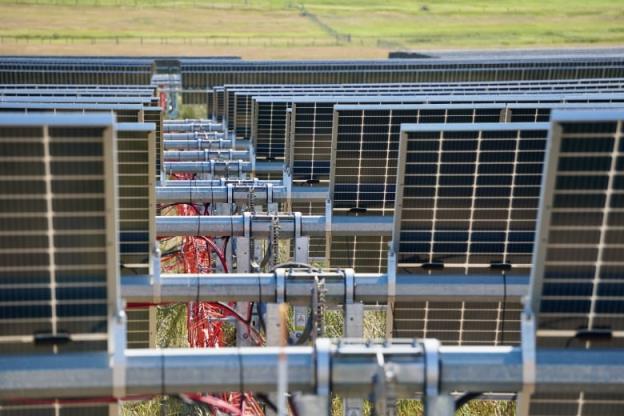 Rows of solar panels are shown with a field in the distance.